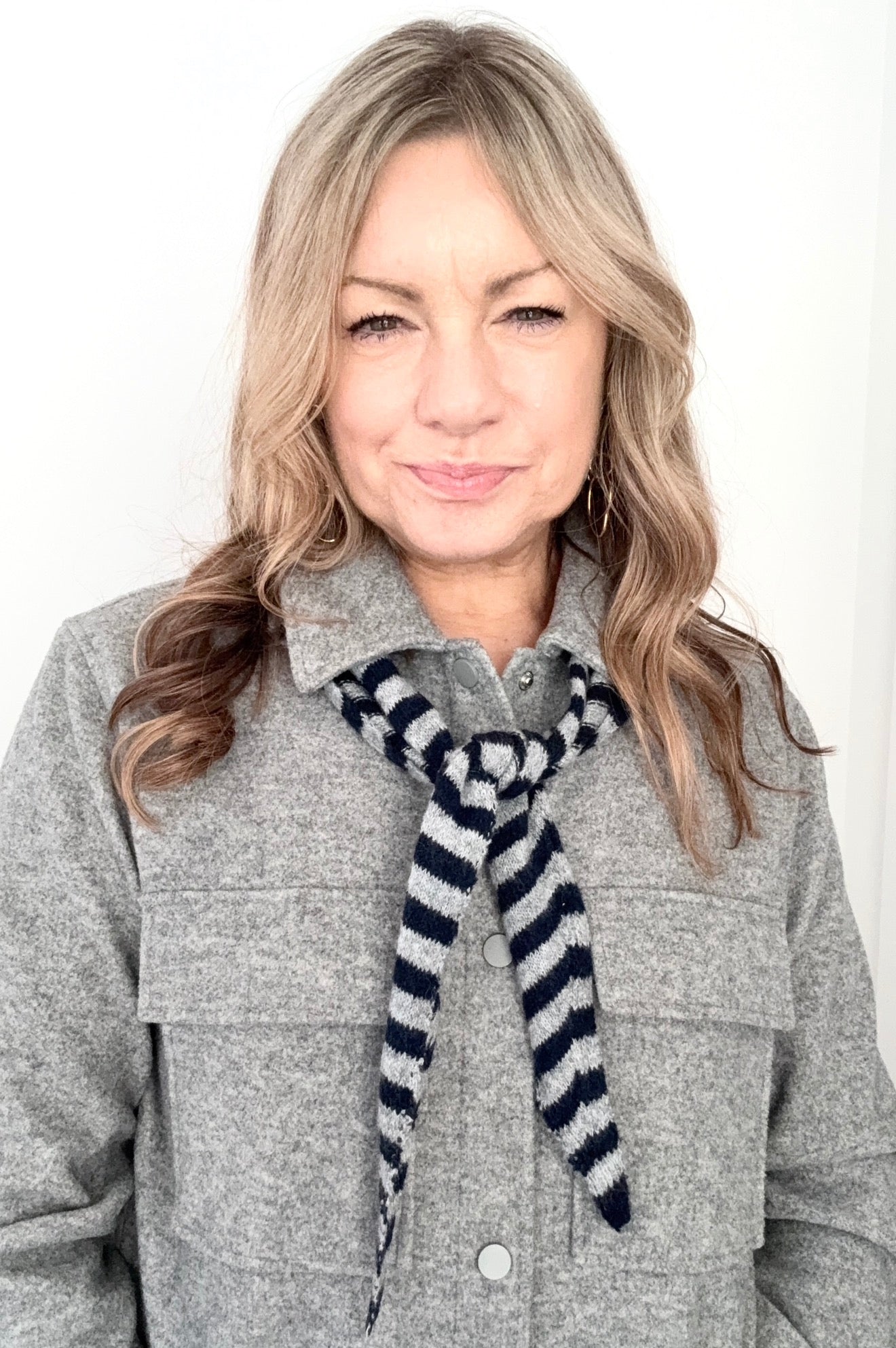 Woman wearing a gray coat and a navy and grey striped scarf against a white background