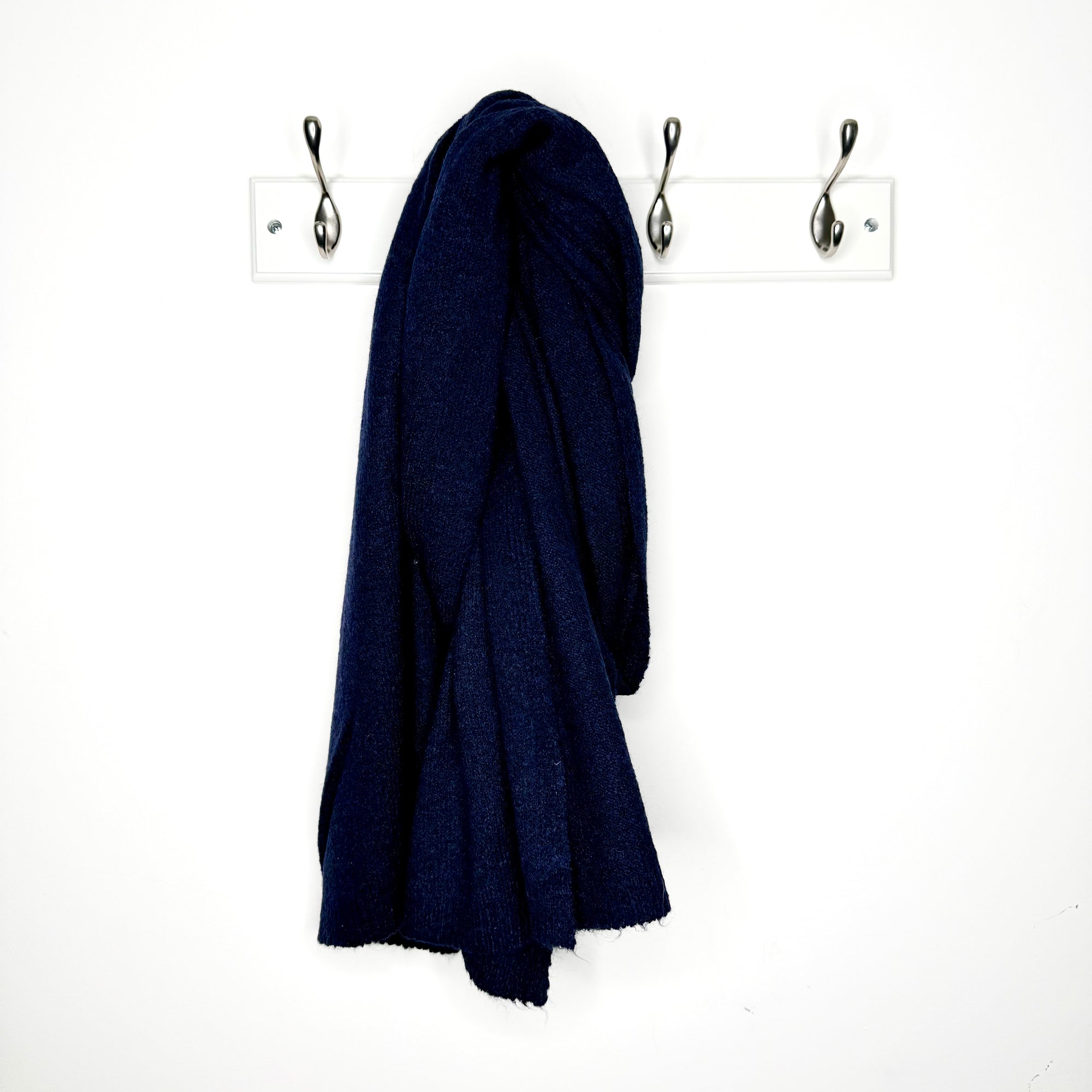 Navy blue knitted scarf hanging on a  peg against a white wall 
