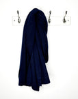 Navy blue knitted scarf hanging on a  peg against a white wall 