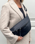 A person wearing a navy blue large crossbody bum bag with silver hardware and an adjustable strap.