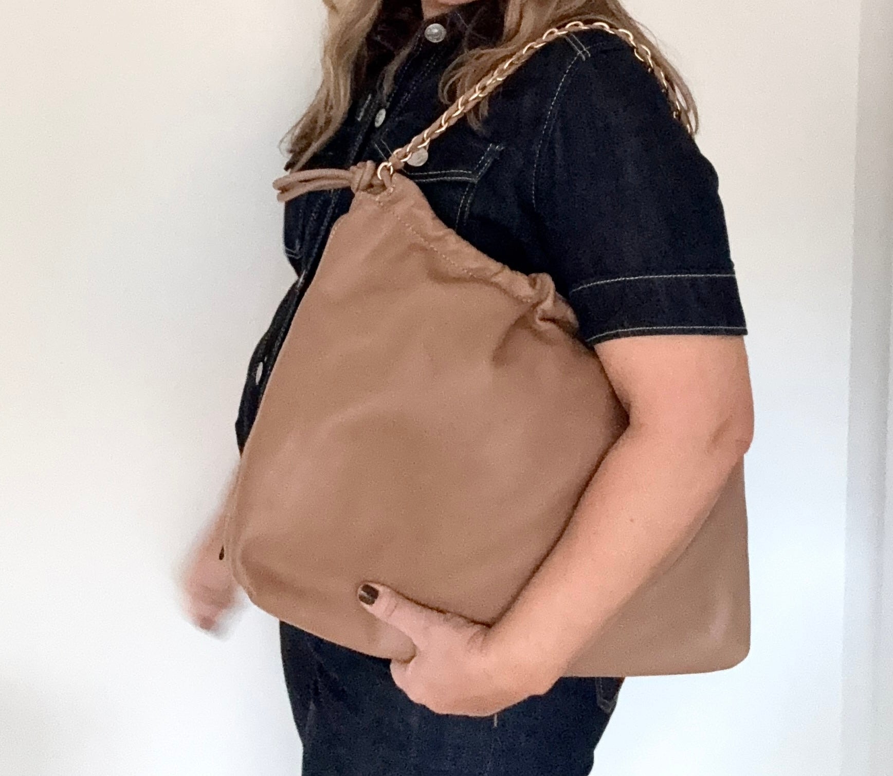 woman holding a pale camel faux leather oversized bag with a gold chain 