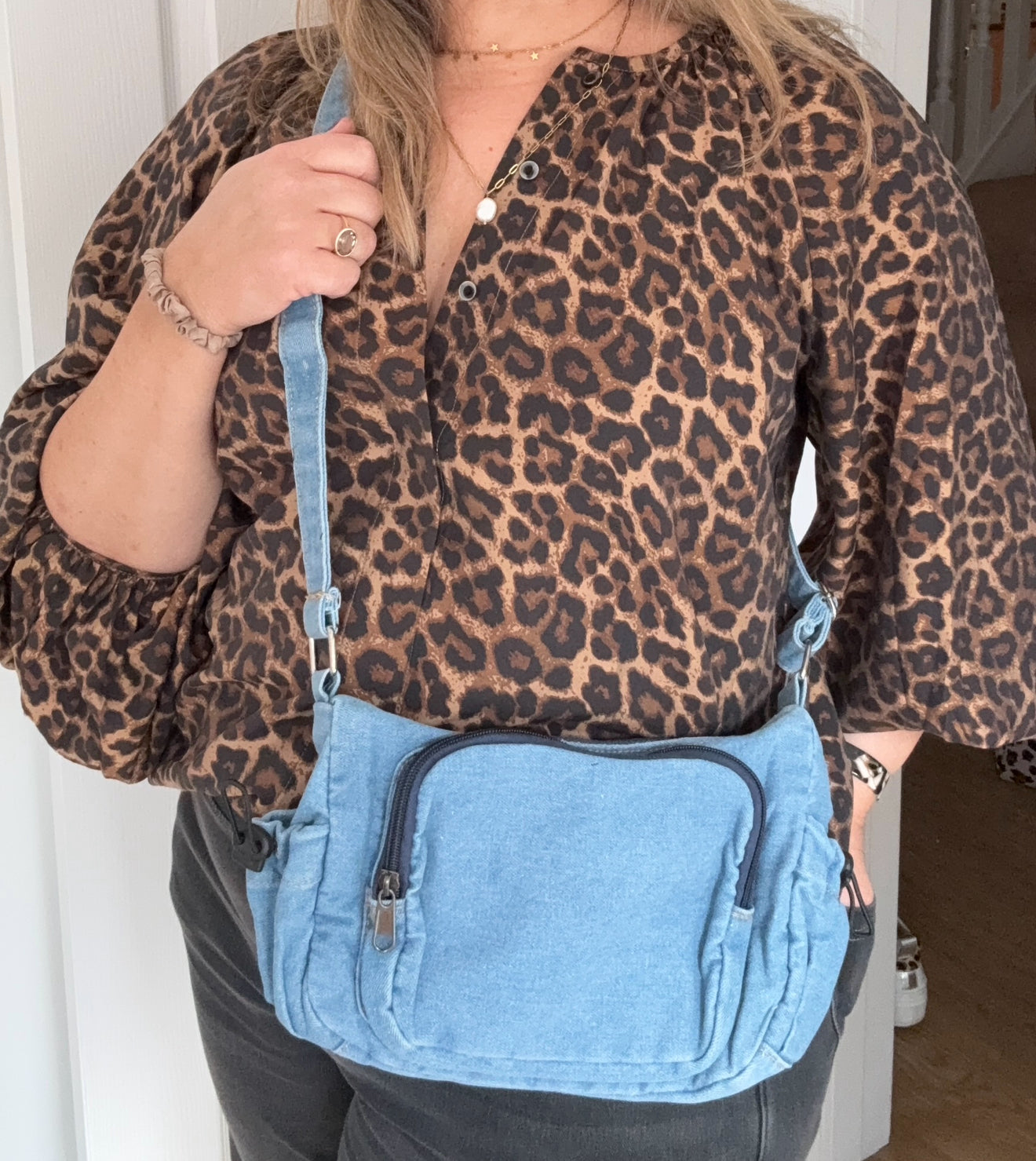 woman wearing a leopard print top and holding a blue denim bag.