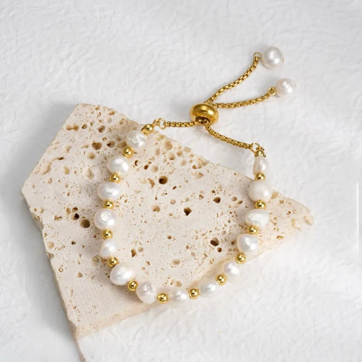 Pearl and gold bracelet on a textured stone surface