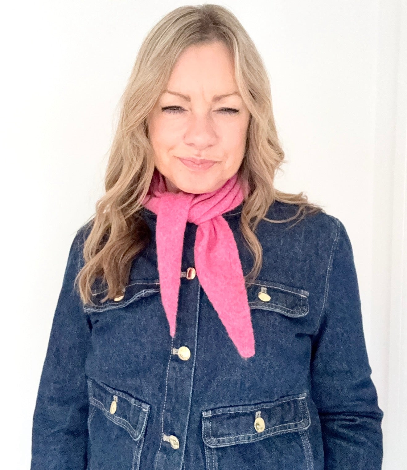 Woman wearing a blue denim jacket and pink scarf against a white background