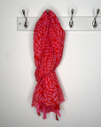 Red and pink patterned scarf hanging on a white wall with hooks