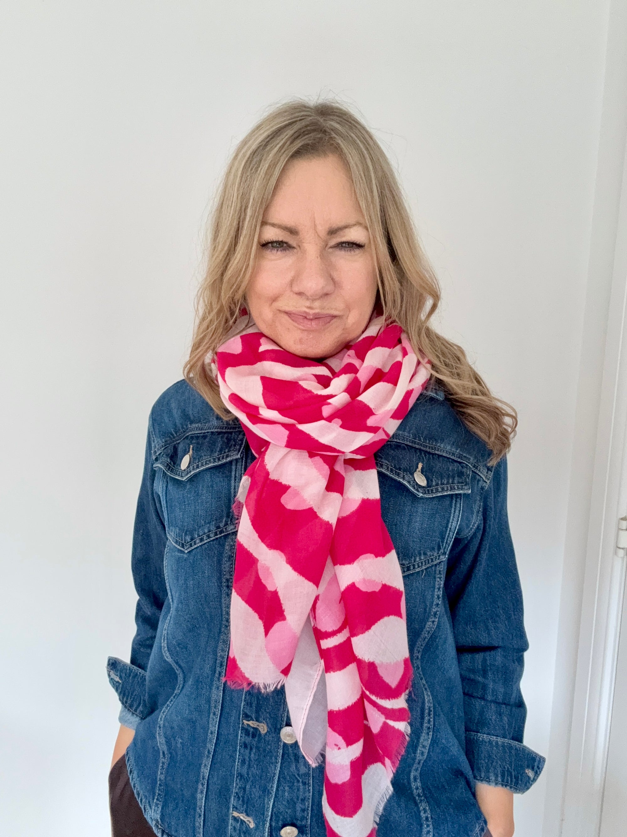 Woman wearing a pink and white patterned scarf with a denim jacket against a white background