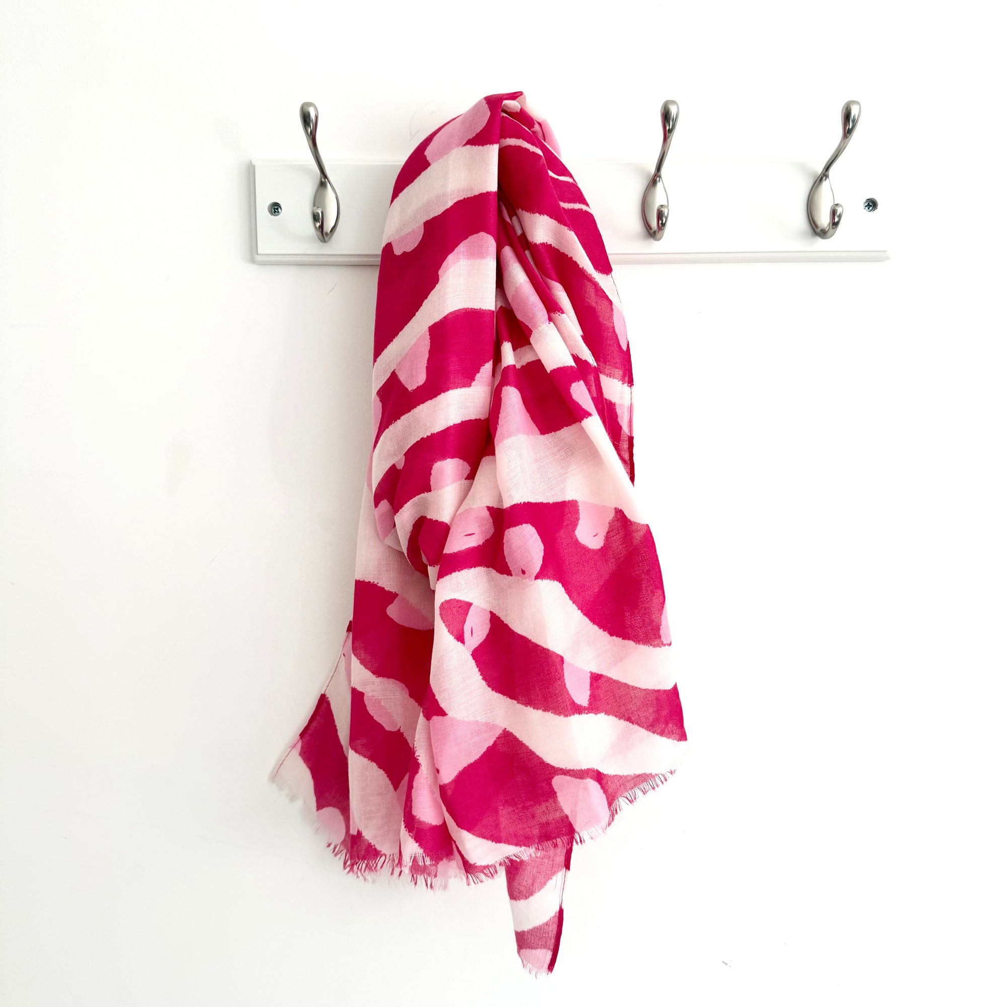 Pink and white patterned scarf draped over a coat rack on a white background