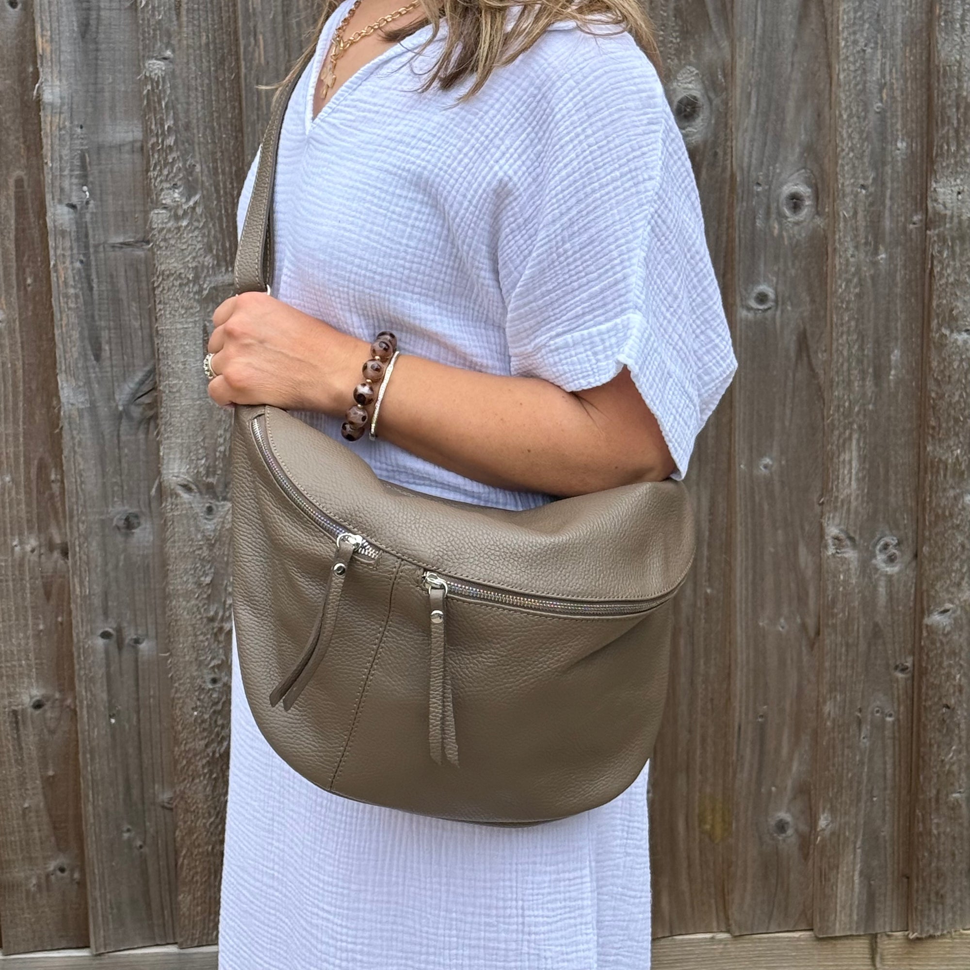 Woman wearing a white dress, holding a dark taupe handbag against a wooden fence background.