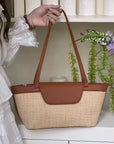 Person holding a brown and tan shoulder summer handbag with a white background and decorative elements.