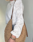Woman wearing a white top, blue jeans, holding a raffia and tan woven crossbody handbag.