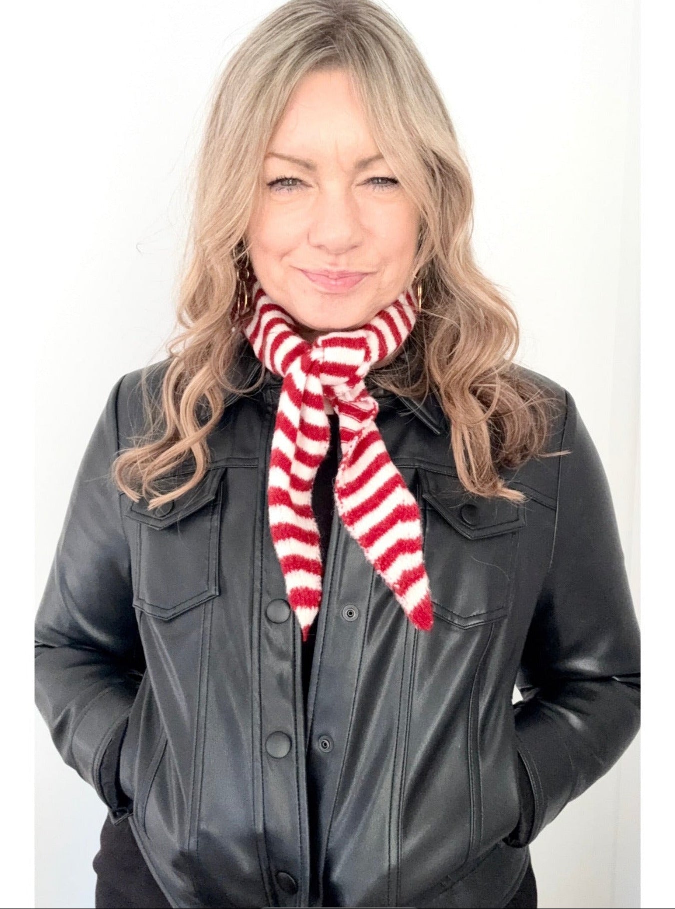 Woman wearing a black jacket and red and white striped scarf on a white background