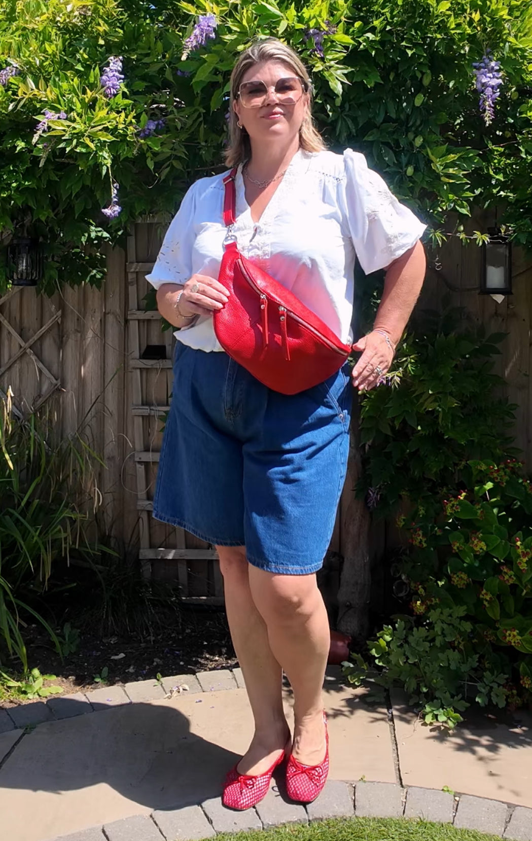 Woman holding a red bag outdoors with greenery in the background