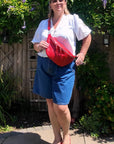 Woman holding a red bag outdoors with greenery in the background