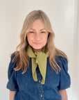 Woman wearing a sage green scarf and blue denim shirt 
