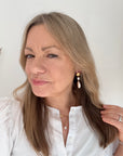 Woman wearing a white blouse with shell and pearl drop earrings.