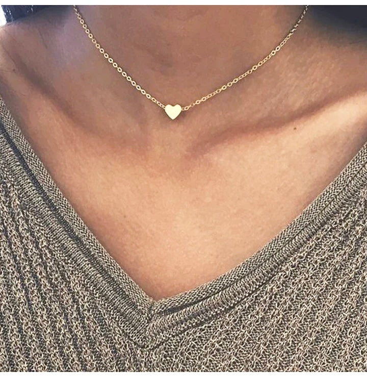 A silver delicate heart necklace worn by a person, featuring a small heart-shaped pendant at the center of the chest.