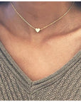 A silver delicate heart necklace worn by a person, featuring a small heart-shaped pendant at the center of the chest.