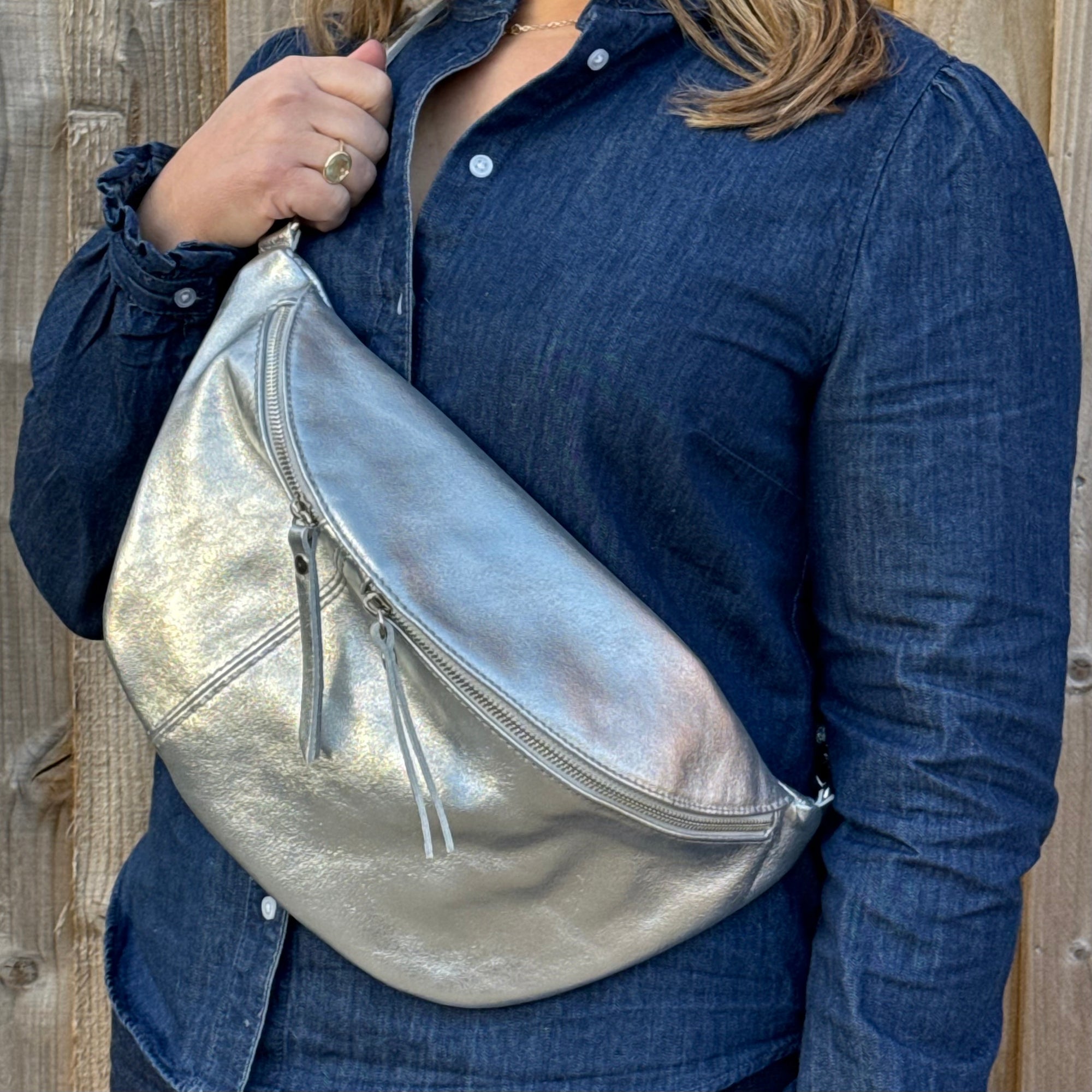 A person wearing a silver large crossbody bum bag with an adjustable, detachable leather strap and multiple zip pockets.