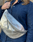 A person wearing a silver large crossbody bum bag with an adjustable, detachable leather strap and multiple zip pockets.