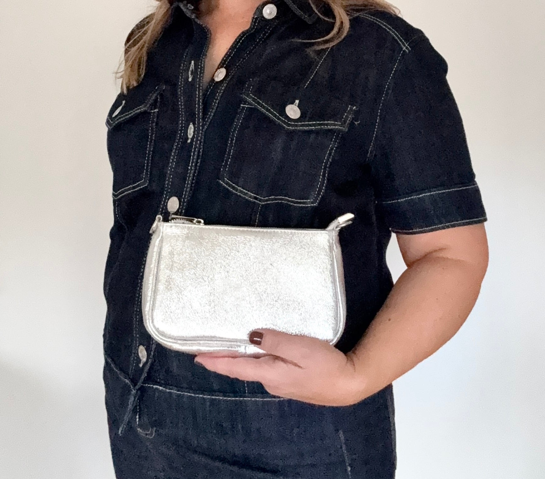 Woman holding a silver glittery leather clutch/ crossbody handbag. 