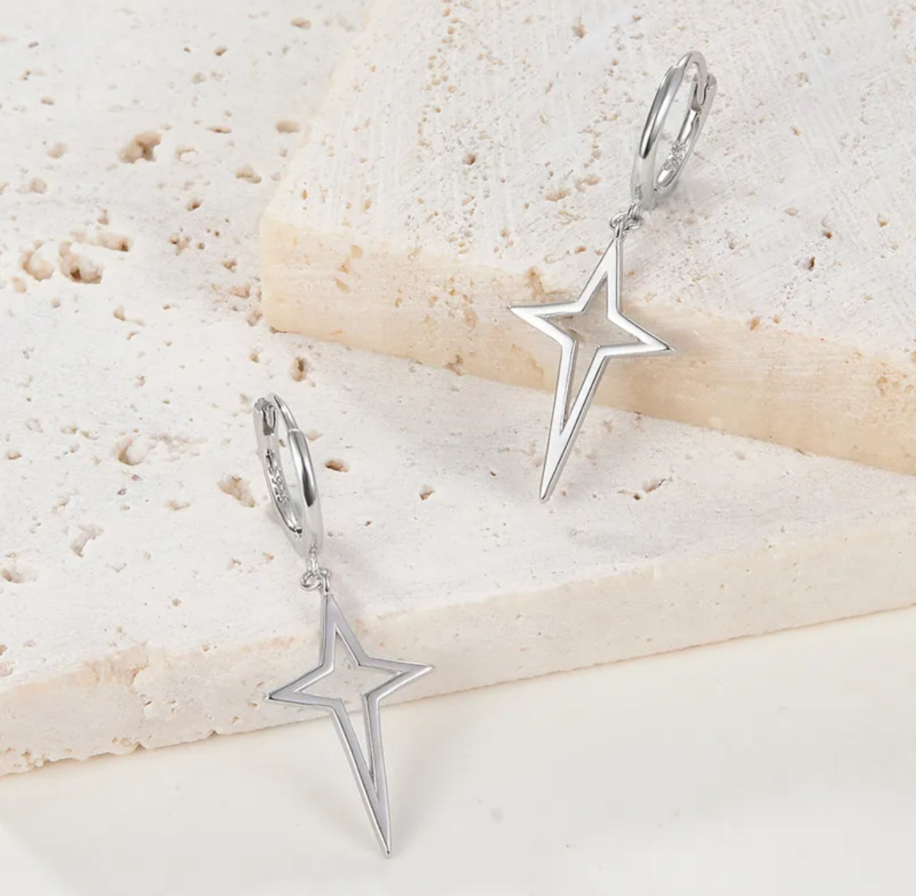 Silver star-shaped earrings on a textured beige surface