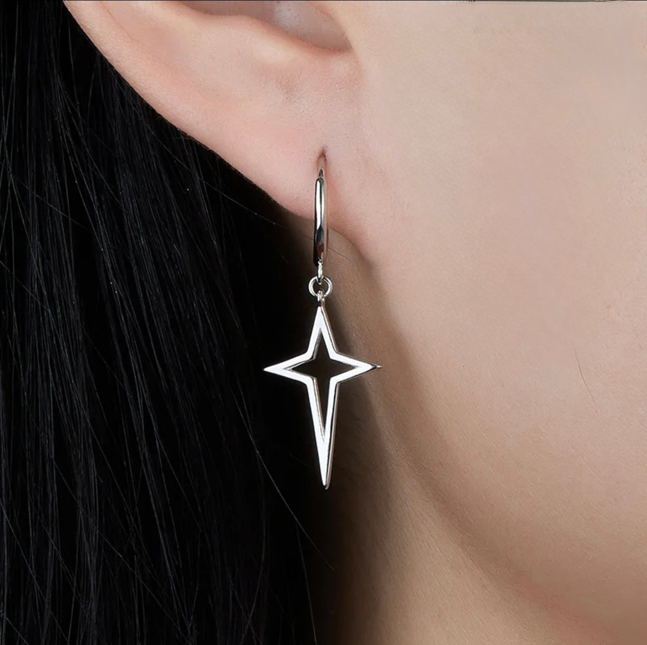Silver star-shaped hoop earring worn by a person with dark hair.
