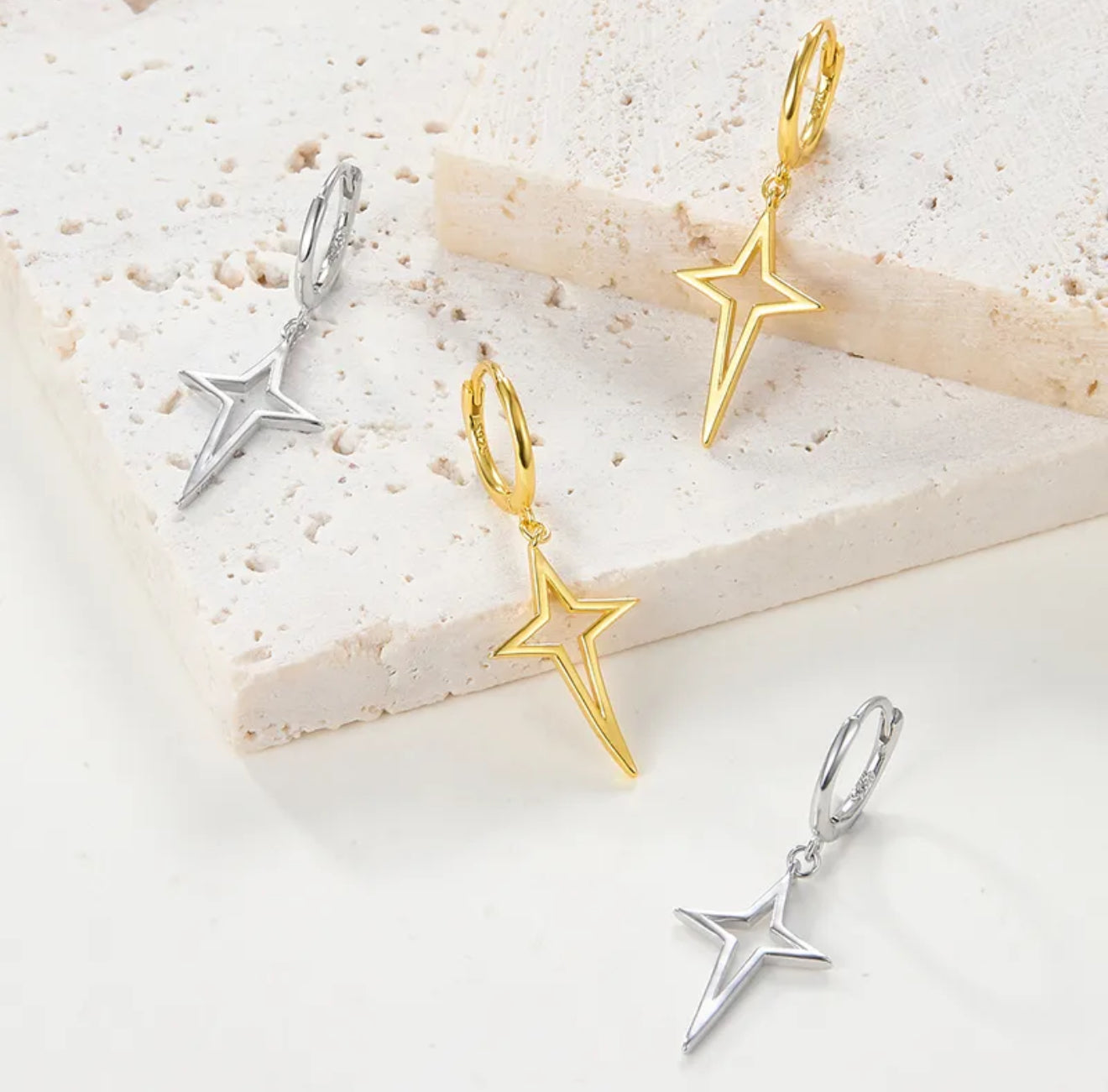 Star-shaped hoop earrings in gold and silver on a light background