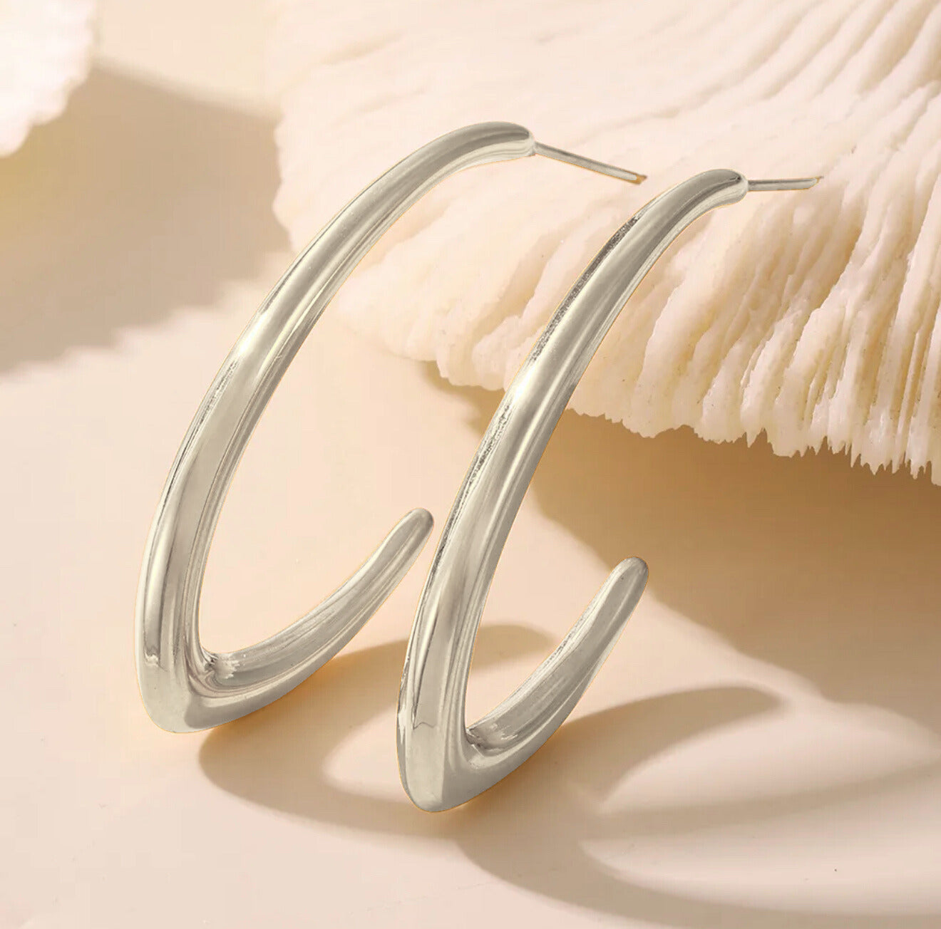 Silver loop drop earrings on a beige background