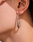 close up of silver loop drop hoop earring worn by a woman 