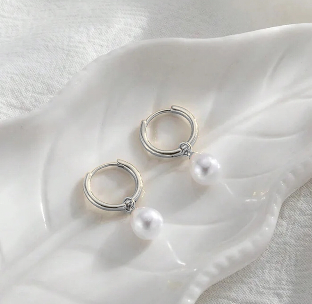 Silver hoop earrings with pearls on a white shell