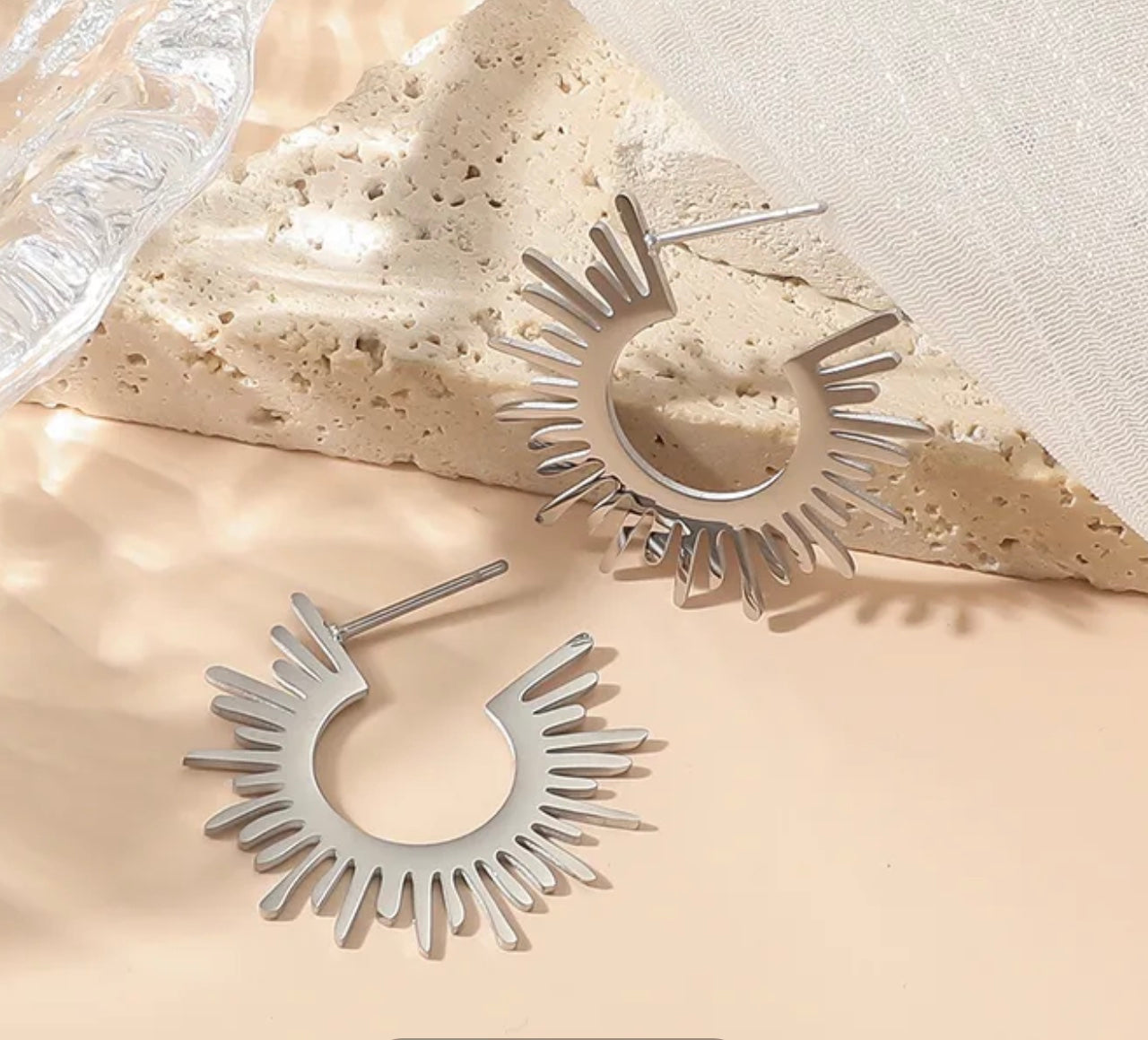 Silver hoop earrings on a textured beige surface.