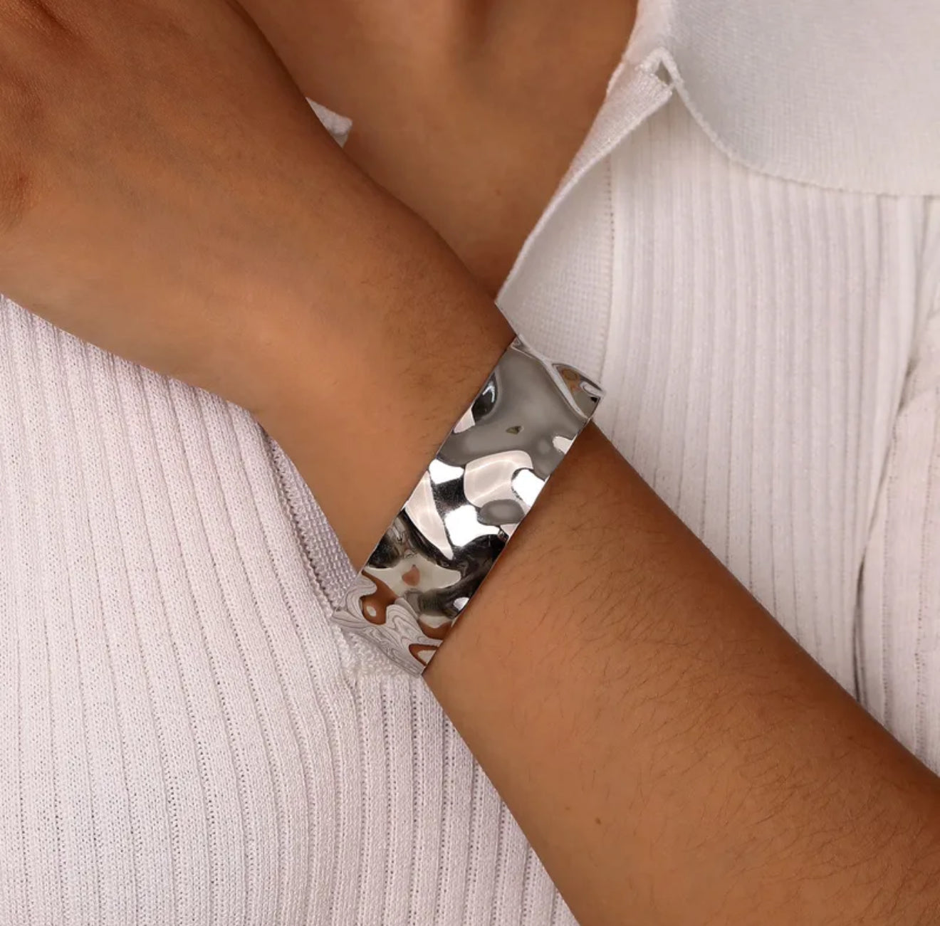 Silver textured cuff bangle bracelet on a wrist against a light background