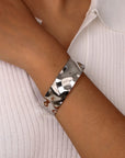 Silver textured cuff bangle bracelet on a wrist against a light background