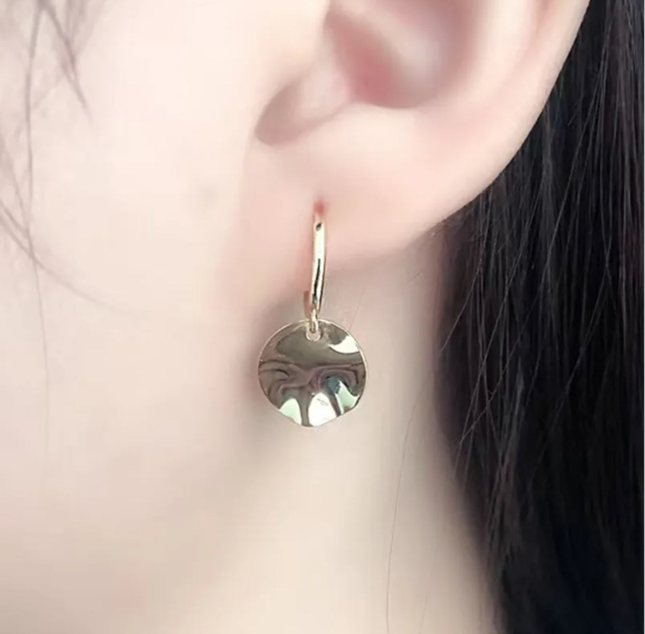 Close up of  a woman wearing silver hoop earring with a round textured disc pendant 