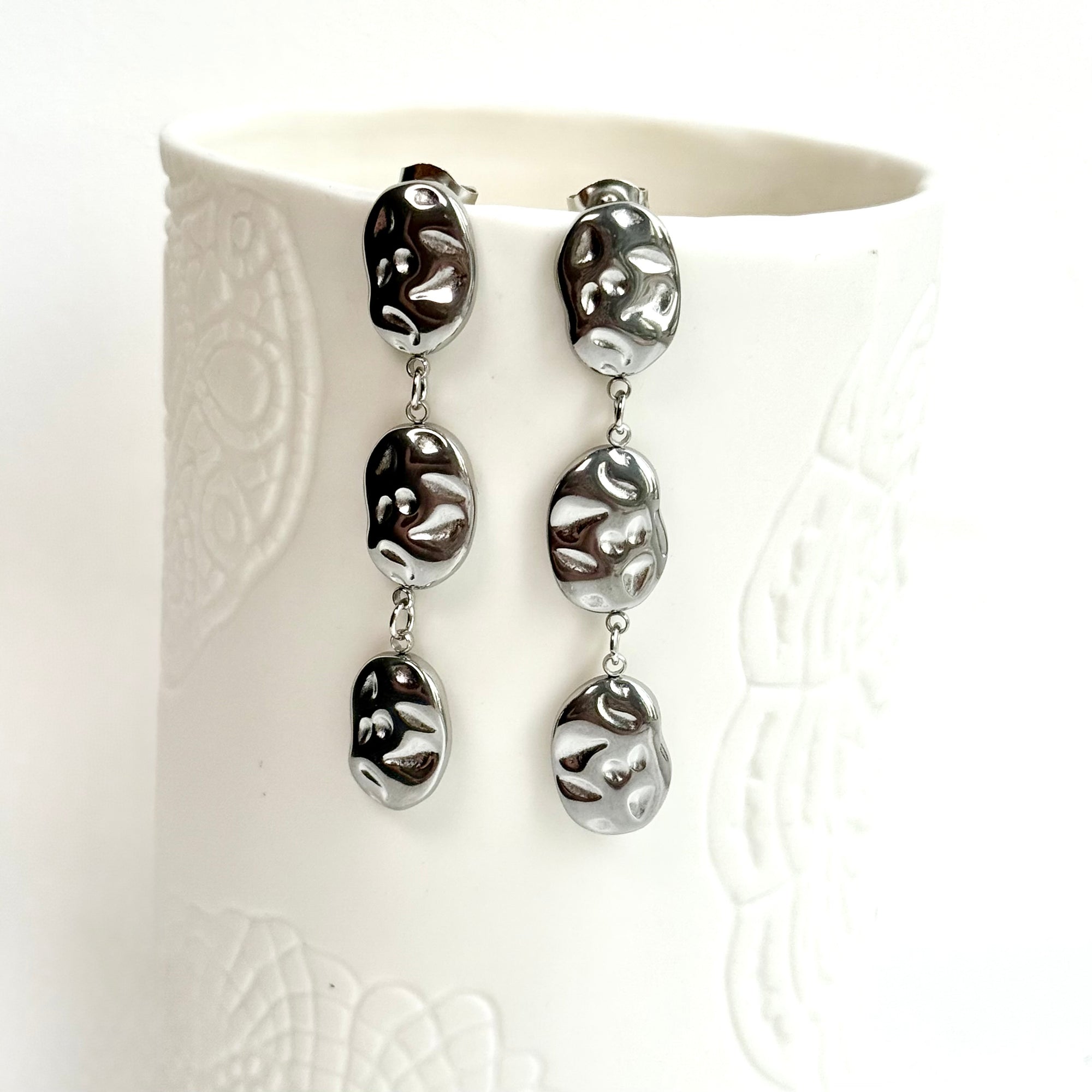Silver triple hammered oval earrings with a textured design on a white cup