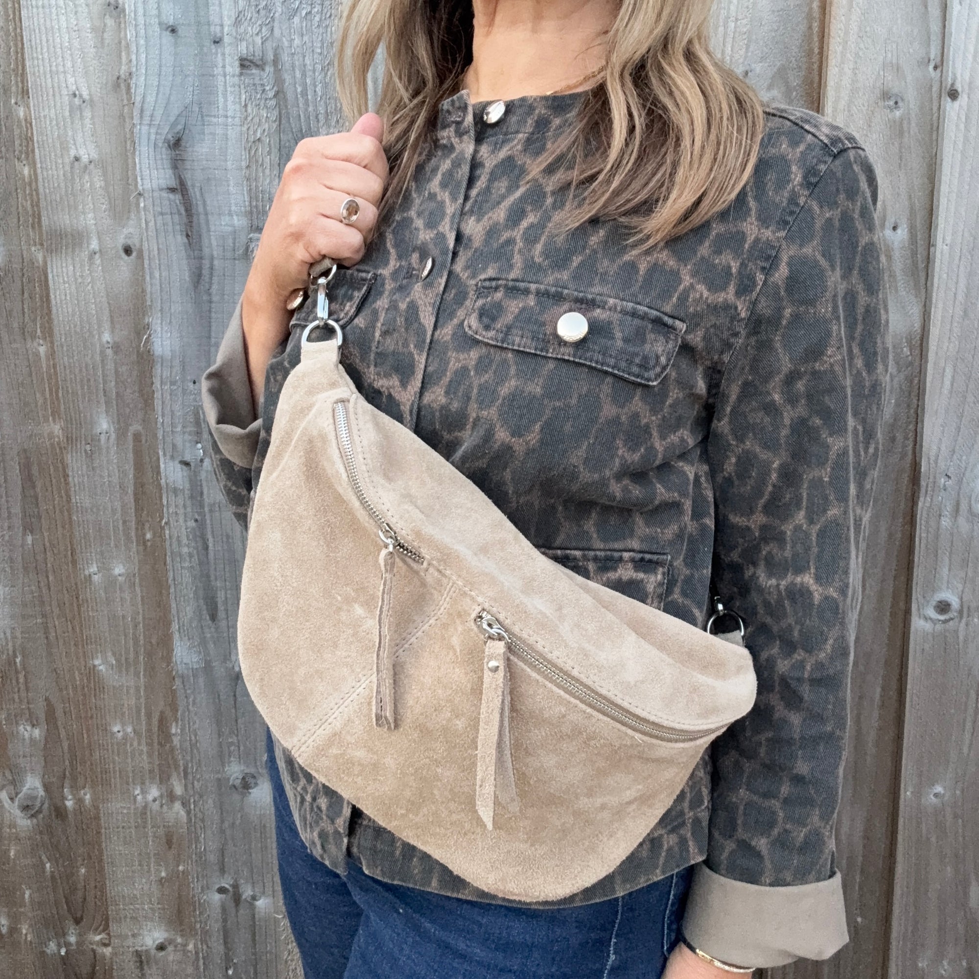 Woman wearing a leopard print jacket holding a stone beige suede crossbody handbag. 