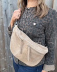 Woman wearing a leopard print jacket holding a stone beige suede crossbody handbag. 
