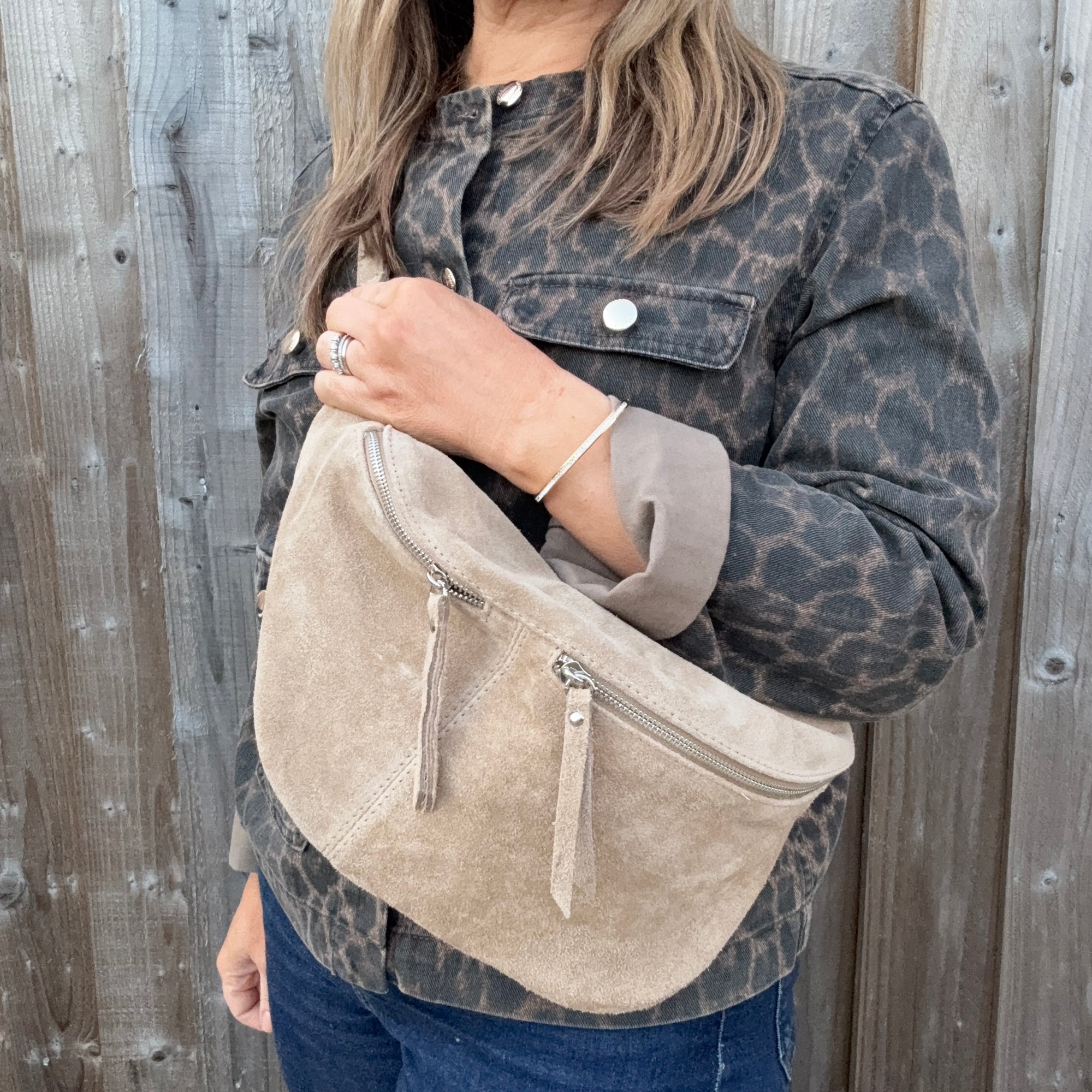 Woman wearing a leopard print jacket holding a stone beige suede crossbody handbag. 