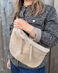 Woman wearing a leopard print jacket holding a stone beige suede crossbody handbag. 