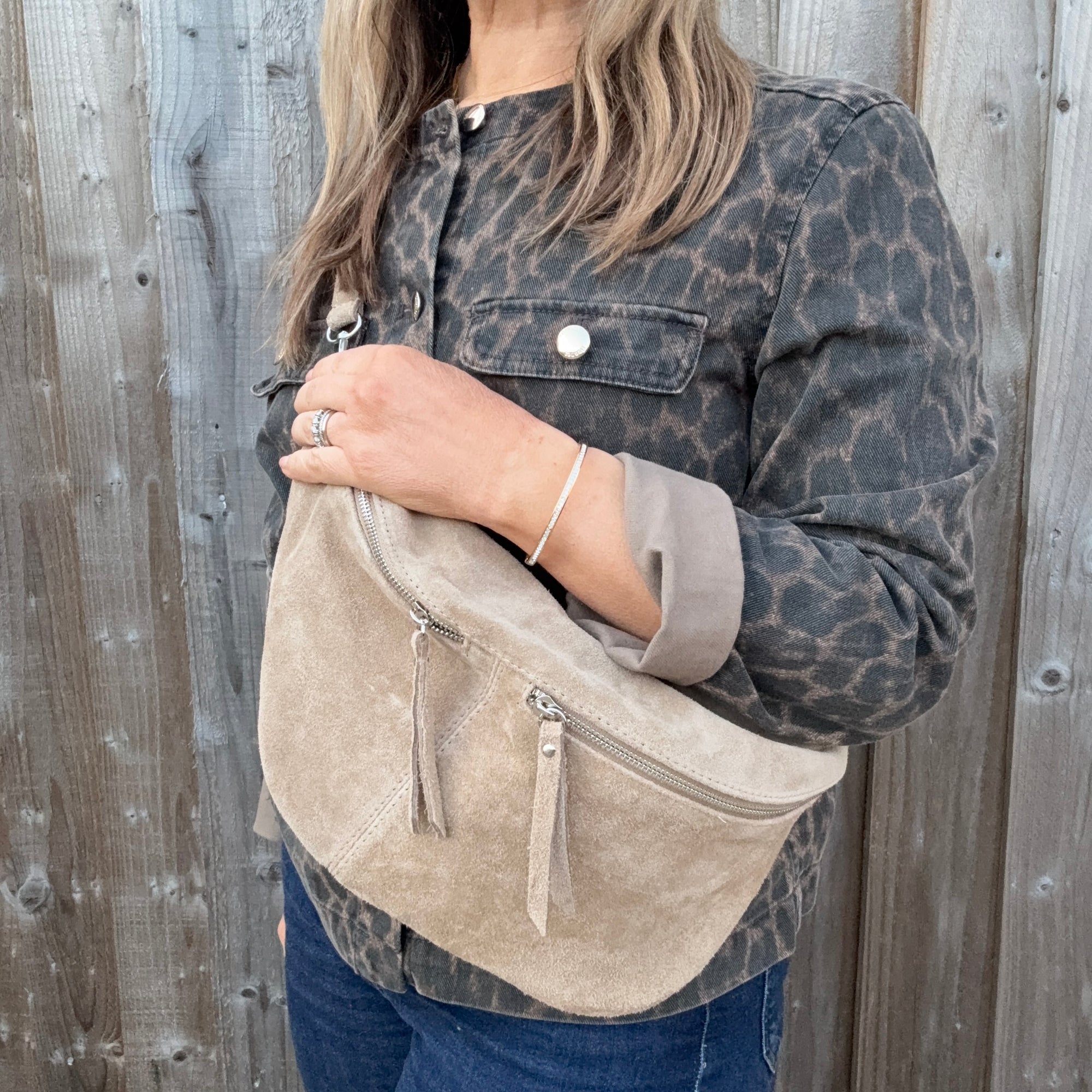 Woman wearing a leopard print jacket holding a stone beige suede crossbody handbag. 