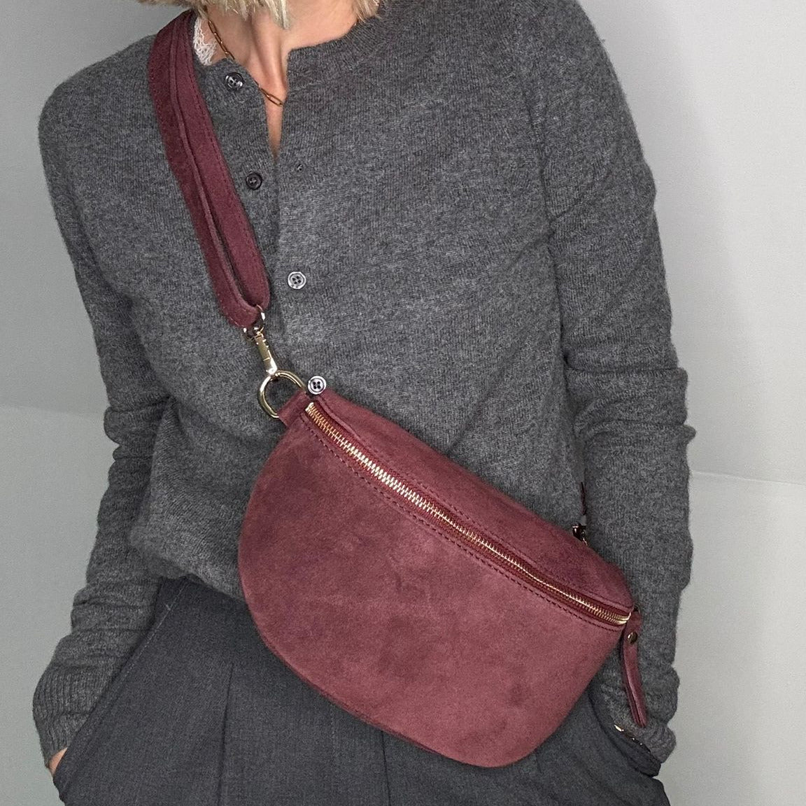 woman  wearing a burgundy suede crossbody bag with detachable strap and gold accents 