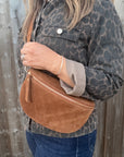 Woman wearing a leopard print jacket holding a dark tan suede bag against a wooden background.