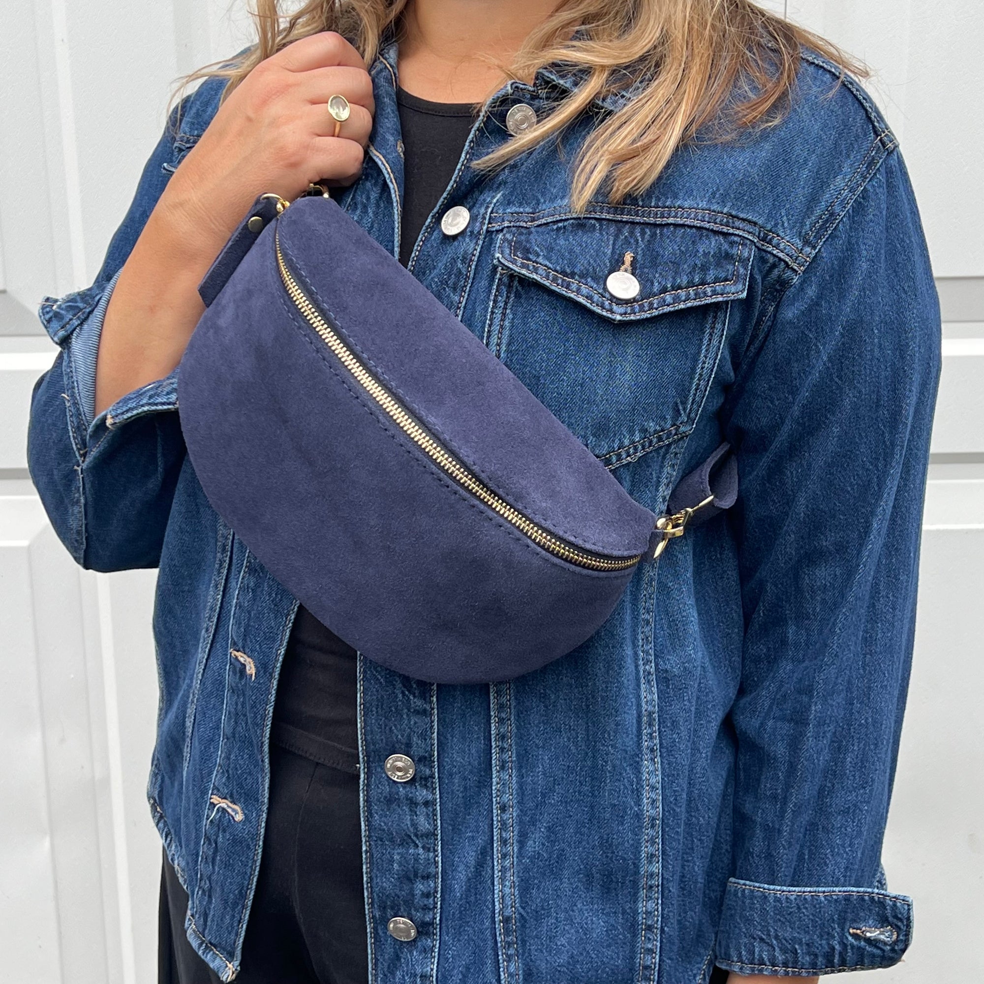 A woman wearing a navy suede leather crossbody bag with a denim jacket and black pants.