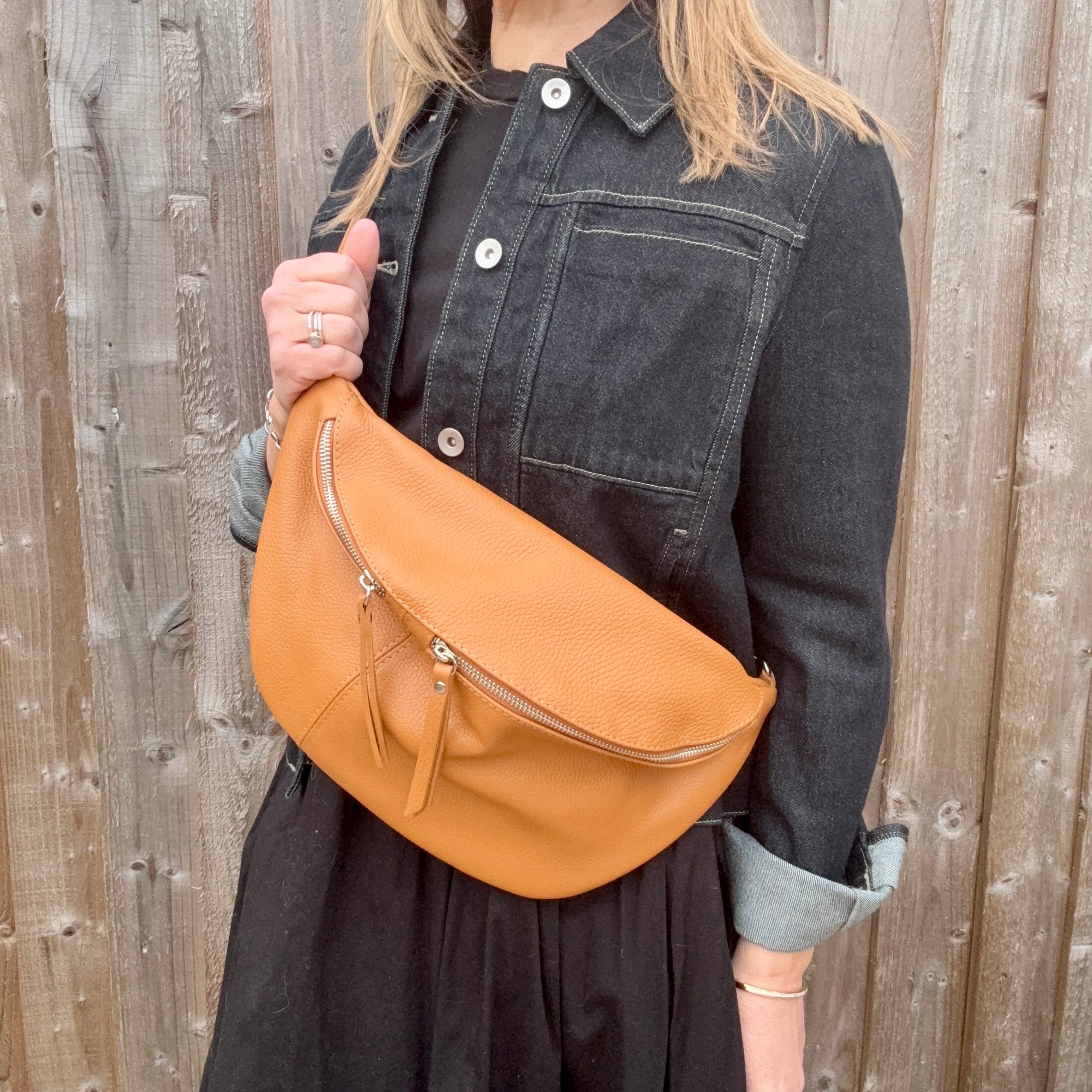 Woman wearing a black and denim jacket, holding a tan leather crossbody handbag.