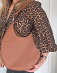 woman wearing a leopard print jacket holding a tan leather bag.