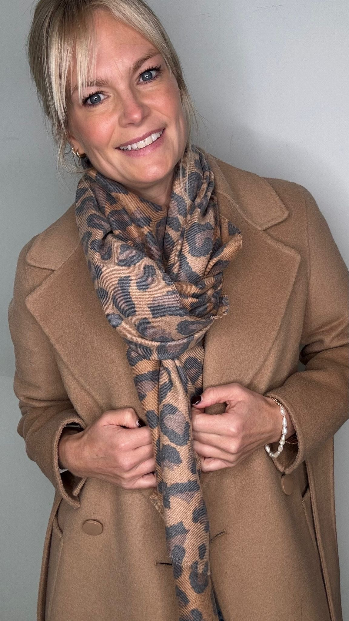 Woman wearing a tan coat and a tan mix  animal print midweight scarf.
