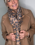 Woman wearing a tan coat and a tan mix  animal print midweight scarf.