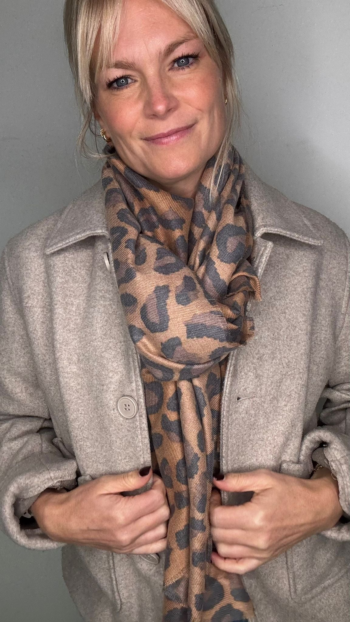 Woman wearing a mixed animal print scarf and beige coat 