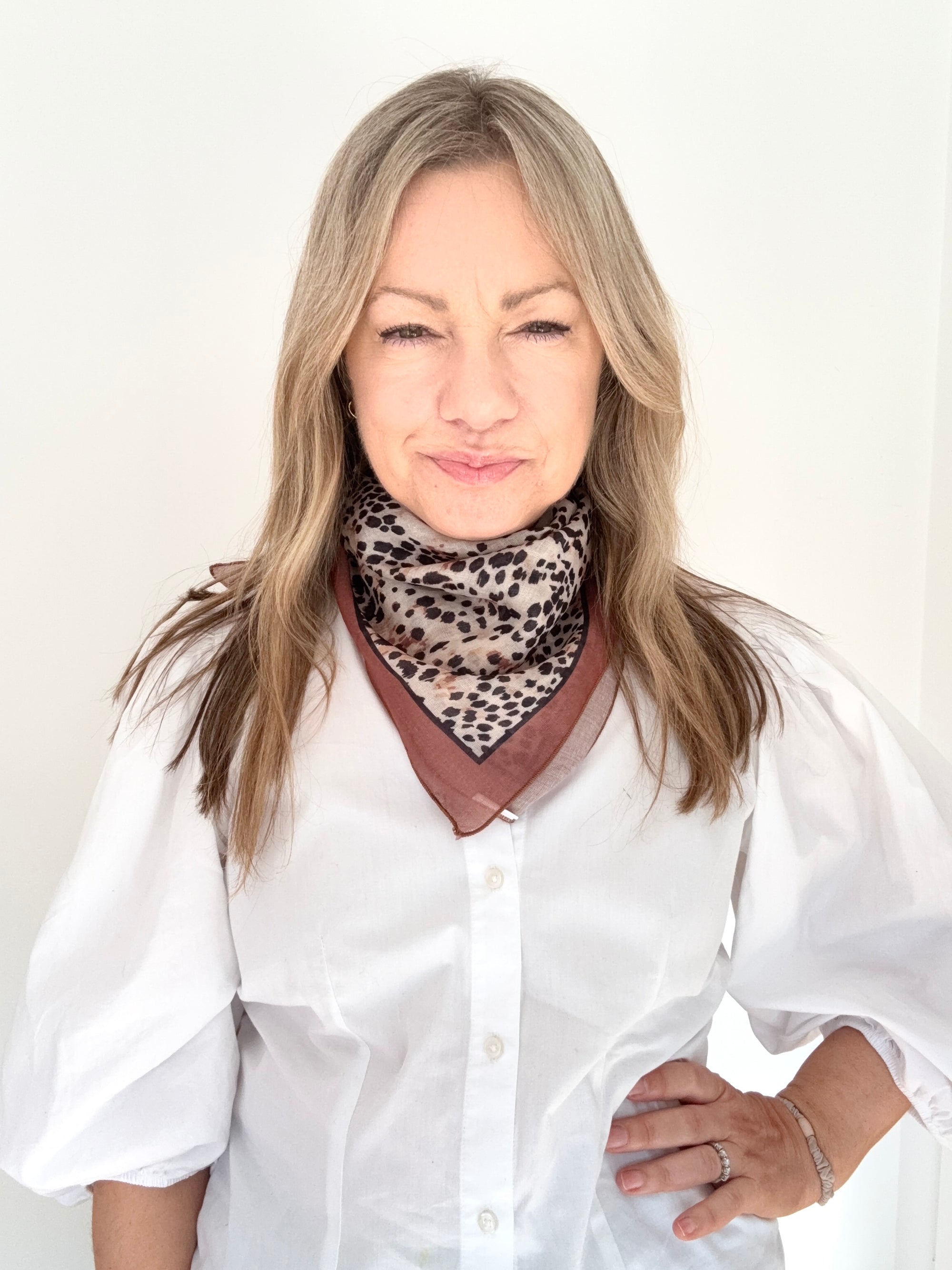 Woman wearing a white shirt and an animal print square scarf. 