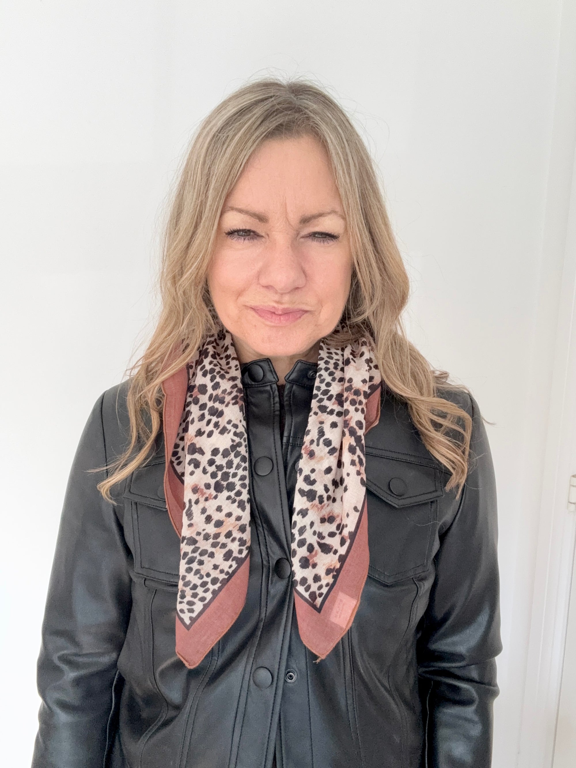 Woman wearing a black leather jacket and a animal print square scarf.